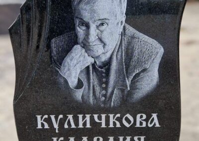 Полированый фигурный памятник из гранита габбро с оформлением. На памятнике художественный портрет женщины и гравировка фамилии, имени и дат.
