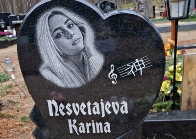 Фигурный гранитный памятник в форме сердца с детальной гравировкой портрета и нотными знаками на кладбище в Таллине.